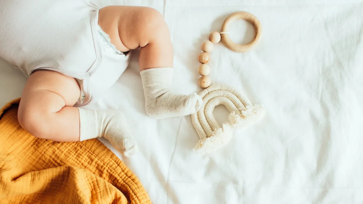 Baby playing with a wooden toy on white linens background. Top view. Copy space.